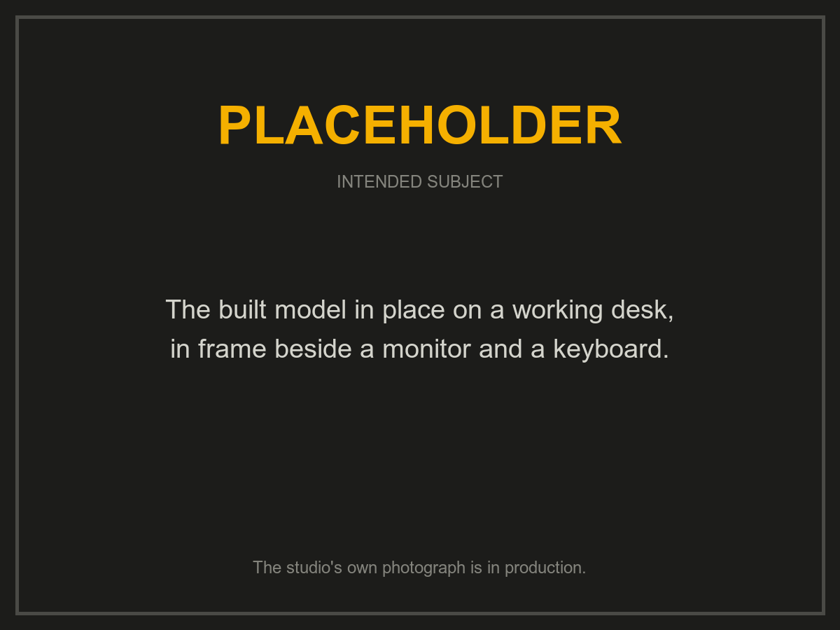 Placeholder: the built model on a working desk, beside a monitor and a keyboard. The studio's own photograph is in production.