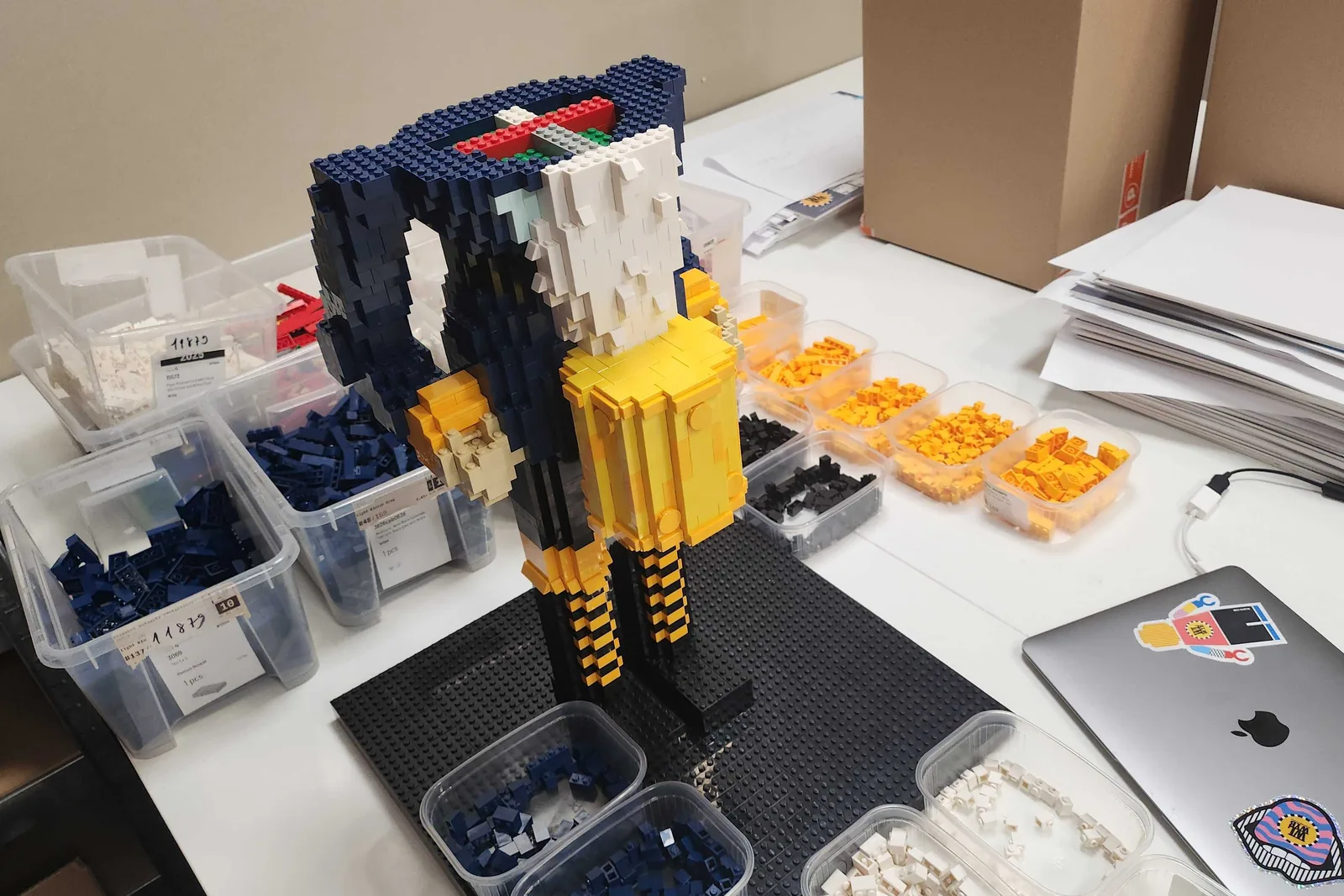 The life-size Nutcracker part-built on its base plate, headless and armless, surrounded by open tubs of navy, white, yellow and black elements sorted for the job.