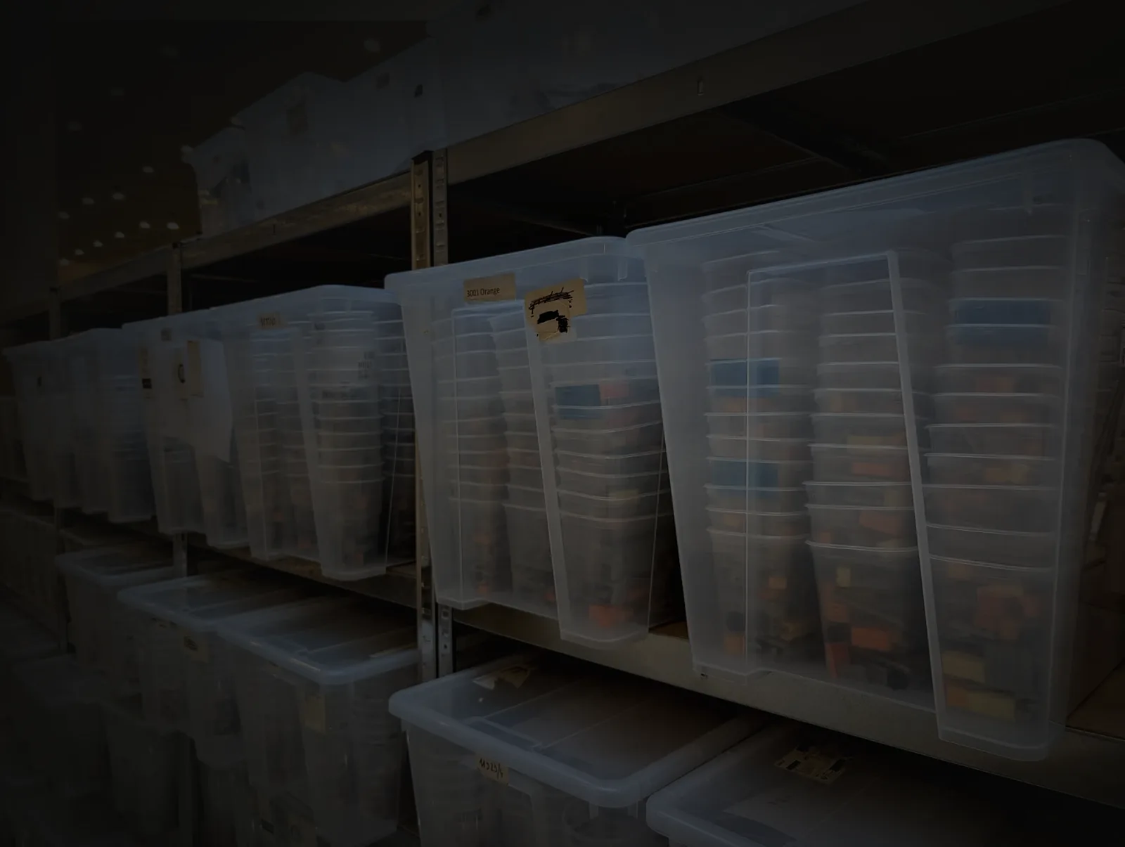 Studio shelving stacked with clear bins, each holding rows of cups of elements sorted by colour and part.