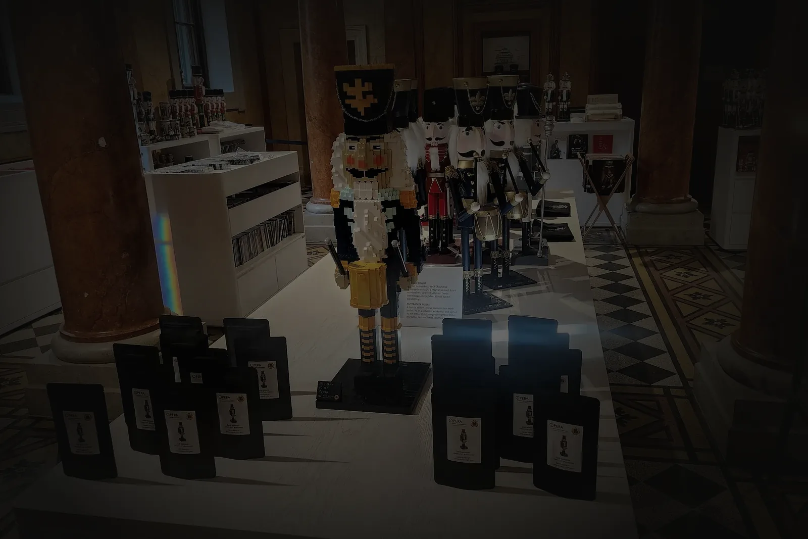 The life-size brick Nutcracker standing in the Opera gift shop between the house's traditional wooden nutcrackers, its retail pouches laid out on the display table in front of it.