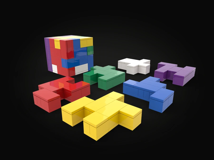 A 3D puzzle built from LEGO® bricks: a finished multicoloured cube beside six interlocking pieces in red, yellow, green, white, blue and purple, laid out apart.