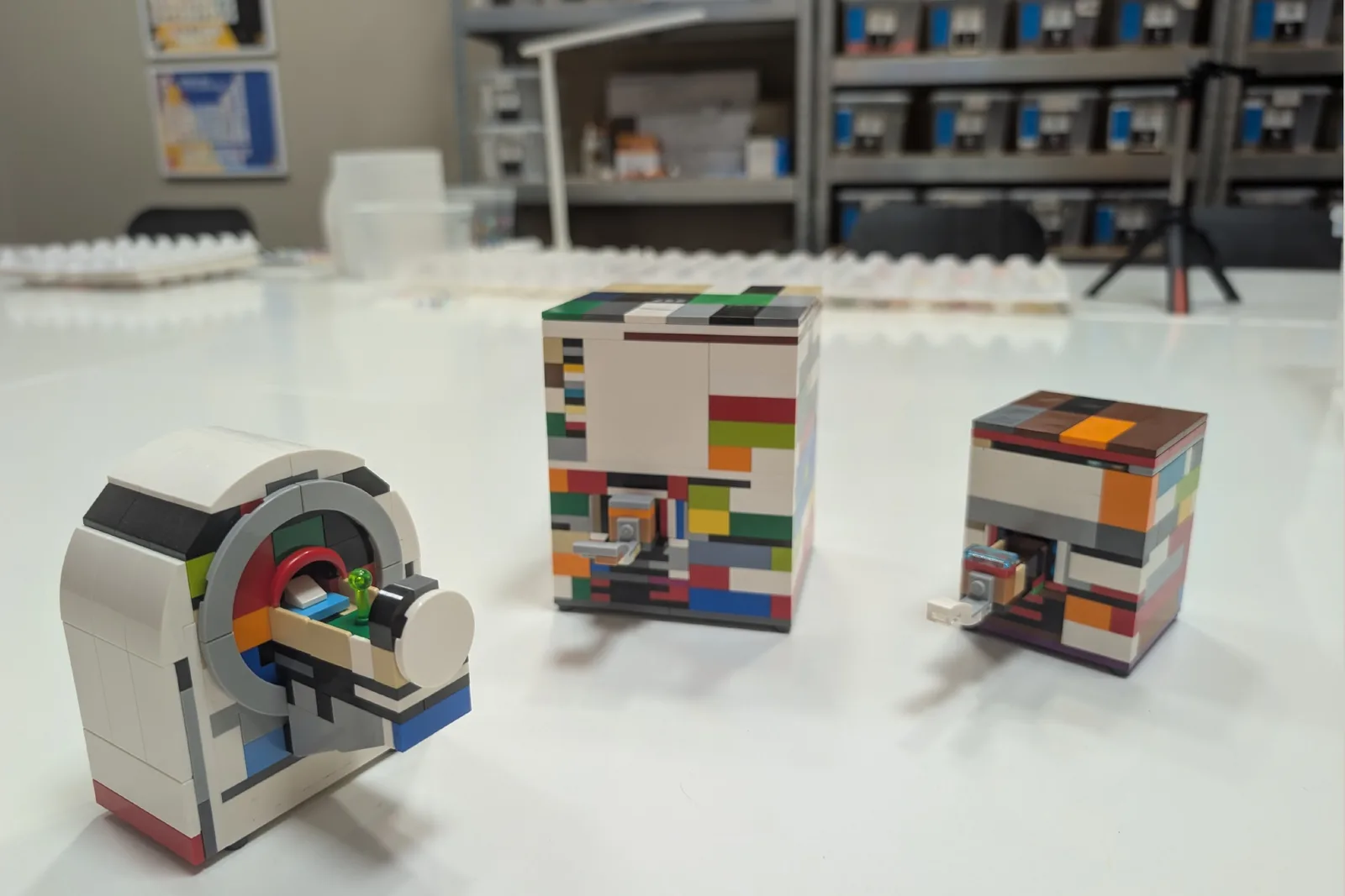 Three scanner prototypes on a workshop bench, each built in clashing mismatched colours, with the parts library racked behind them.